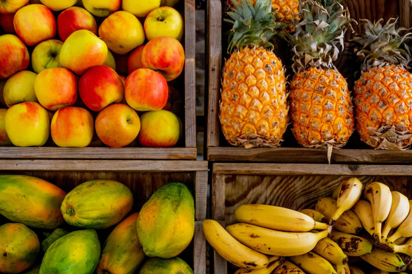 Apples, pineapples, bananas and papayas displayed in wooden crates at a market