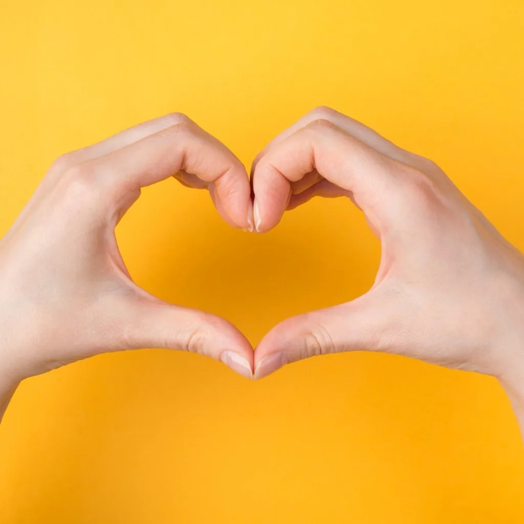 Two hands forming a heart shape against a yellow background