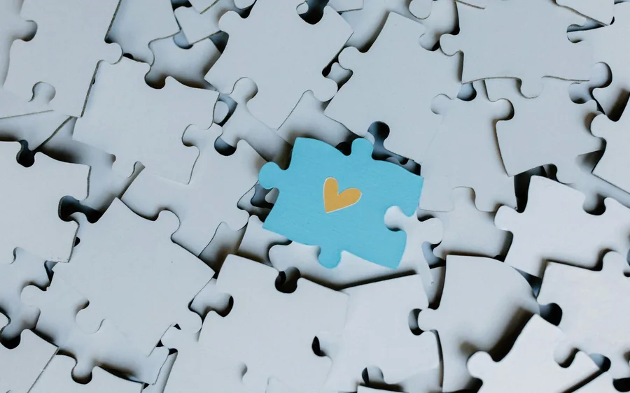 A single blue puzzle piece marked with a heart among plain white puzzle pieces